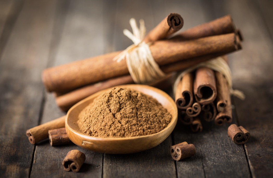 A bowl of ground cinnamon surrounded by cinnamon quils