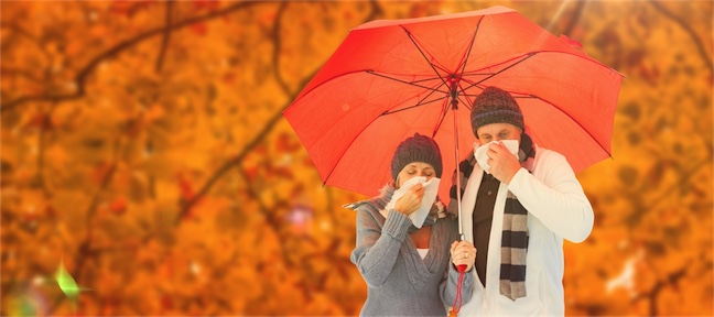 man and woman under umbrella with head colds sneezing into handkercheif