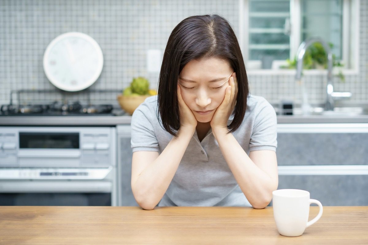 Woman with perimenopause fatigue at kitchen bench with coffee cup.