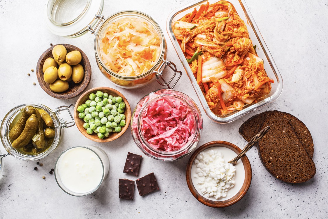 Probiotics food background. Kimchi, beet sauerkraut, sauerkraut, cottage cheese, olives, bread, chocolate, kefir and pickled cucumbers in glass jars, white background, top view.