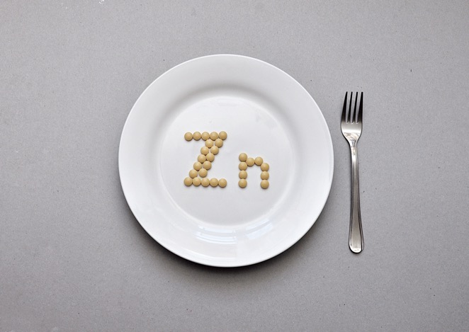 A white plate with Zn spelled out with zinc capsules. A fork is on the right hand side