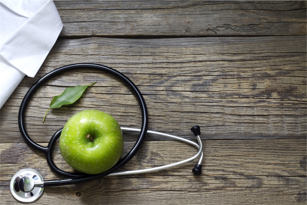 Green apple and stethescope on woooden table